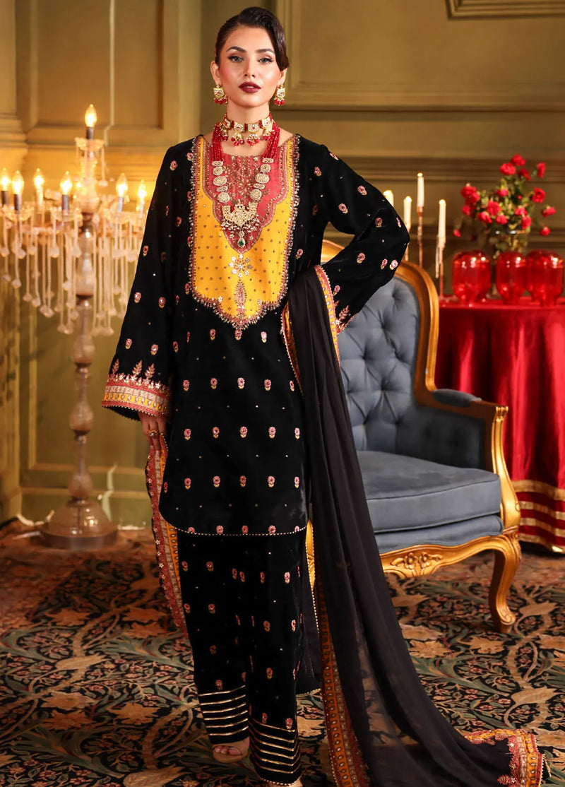 A woman wearing an embroidered black and gold velvet unstitched 3-piece suit with a dupatta.