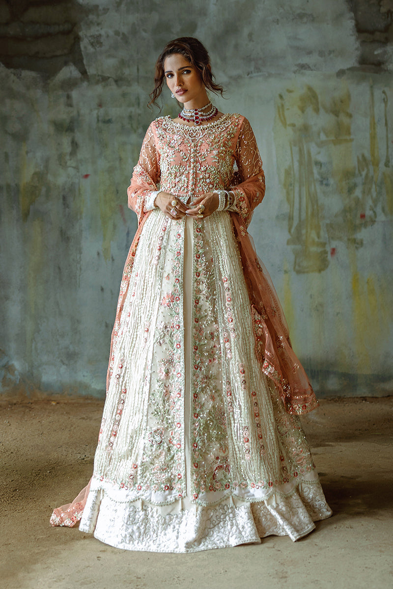A woman wearing a traditional, embroidered, cream-colored gown with floral patterns and a net border, paired with a sequined and embellished lehenga.