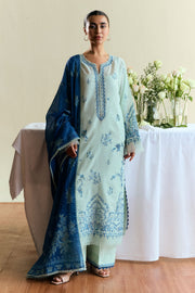 Woman wearing a light blue embroidered dress with a matching dupatta in a decorated room.