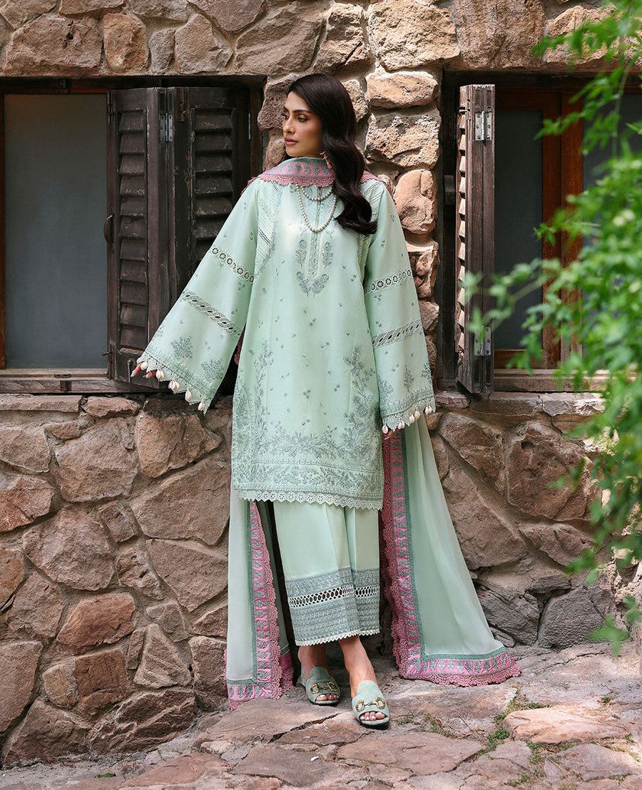Woman in a light green embroidered outfit standing in front of a stone building.