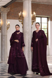 Two women in dark purple traditional outfits standing in a grand hall with columns and chandeliers.