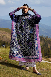 Woman in a traditional outfit with floral patterns standing in a scenic outdoor setting with mountains and greenery.