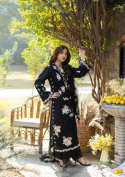 Woman in a black floral dress standing outdoors near a tree and bench.