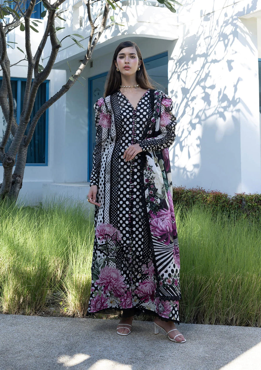 Woman wearing a long, patterned dress standing outdoors with a white building and blue door in the background.