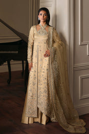 Woman in a traditional beige and gold outfit standing in a room with a piano.