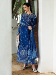 Woman in a blue embroidered outfit standing in a doorway.