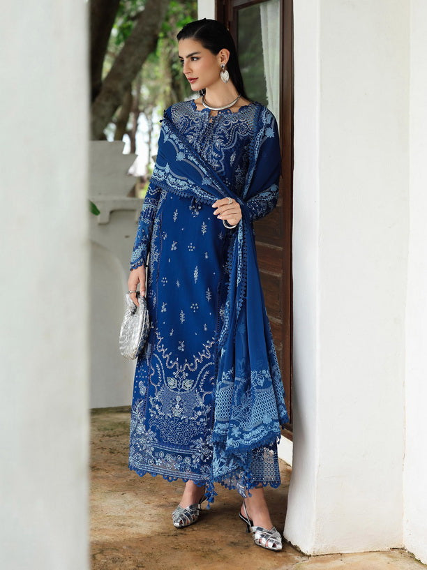 Woman in a blue embroidered outfit standing in a doorway.
