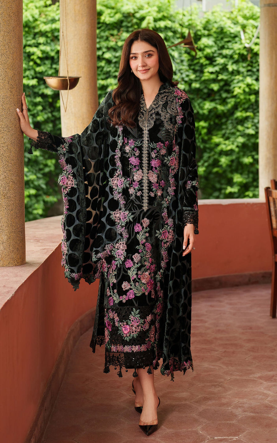 Woman in a black floral dress standing outdoors with greenery in the background