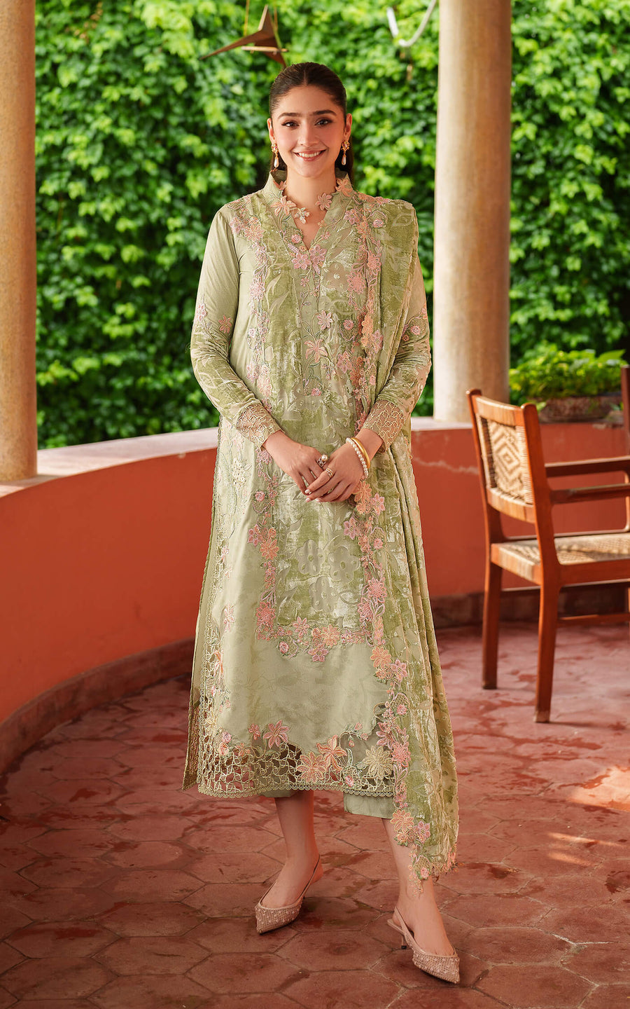 Woman in a light green traditional outfit standing outdoors with greenery in the background