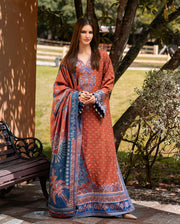Woman in a traditional outfit with a patterned shawl standing outdoors near a tree.