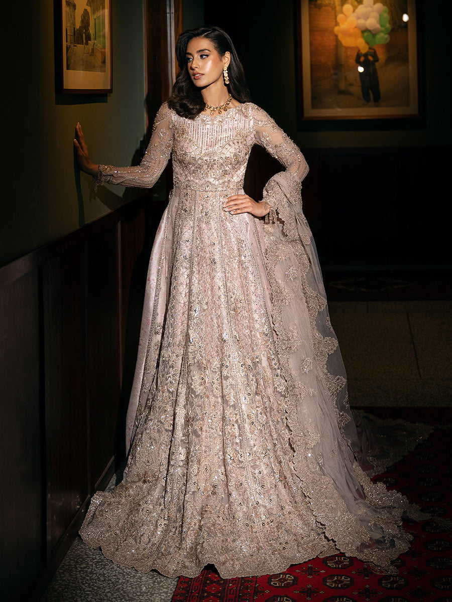 A woman wearing a traditional, embellished, three-piece suit with a net fabric and sequins, in a semi-stretched position, with her hand on the wall.