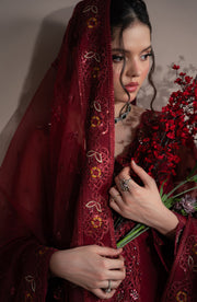 Woman in a red embroidered garment holding flowers against a neutral background