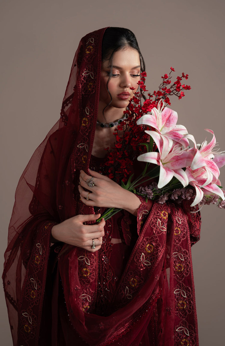 Woman in a red embroidered outfit holding flowers against a brown background
