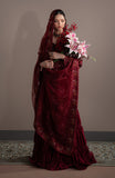 Woman in a burgundy velvet saree holding flowers against a plain background