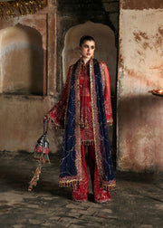 Woman in traditional red and blue outfit with intricate patterns in a rustic setting