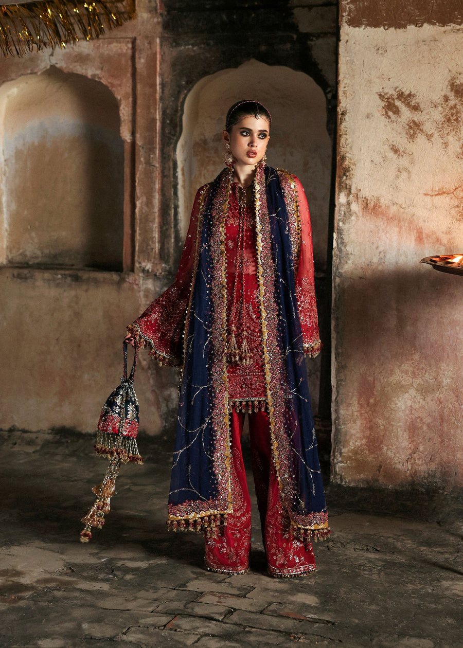 Woman in traditional red and blue outfit with intricate patterns in a rustic setting
