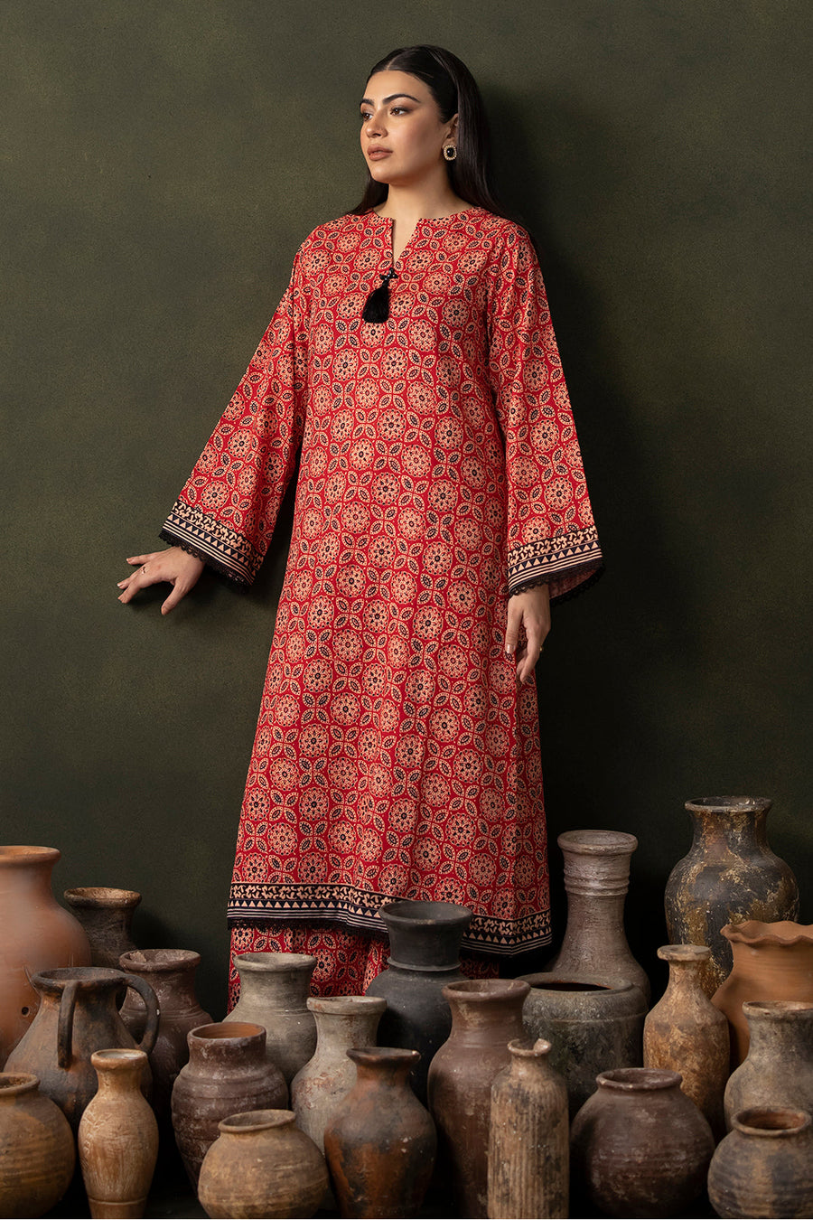 Woman in a red patterned dress standing among ancient pots against a dark background