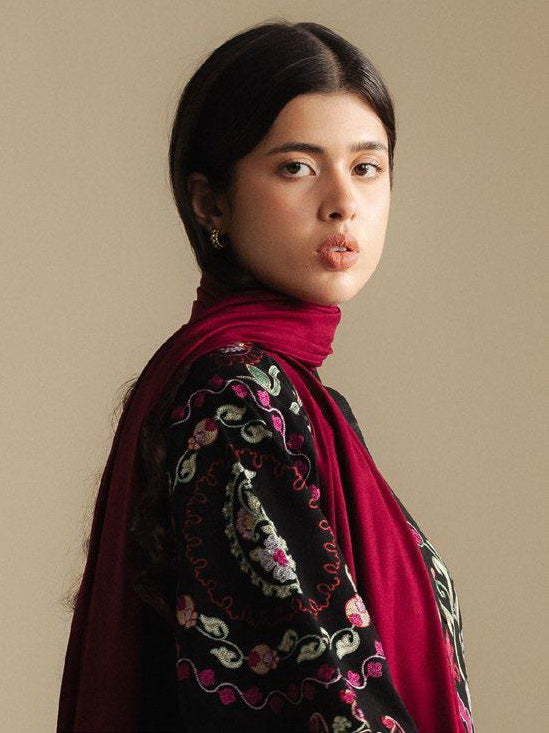Woman wearing a patterned shawl over a dark top against a beige background